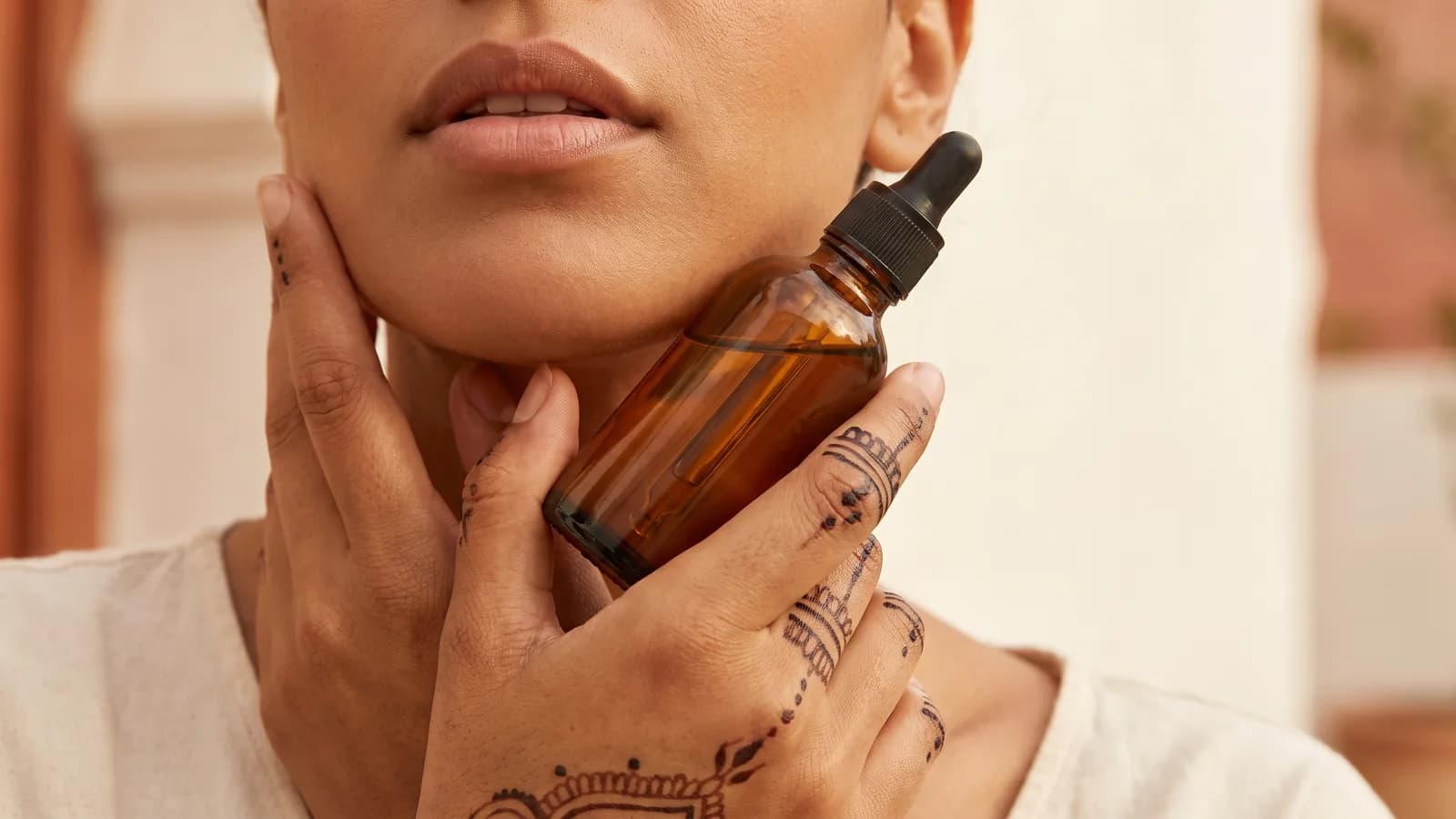 Gros plan sur les mains ornées de henné d’une mannequin marocaine tenant un flacon compte-gouttes en verre ambré