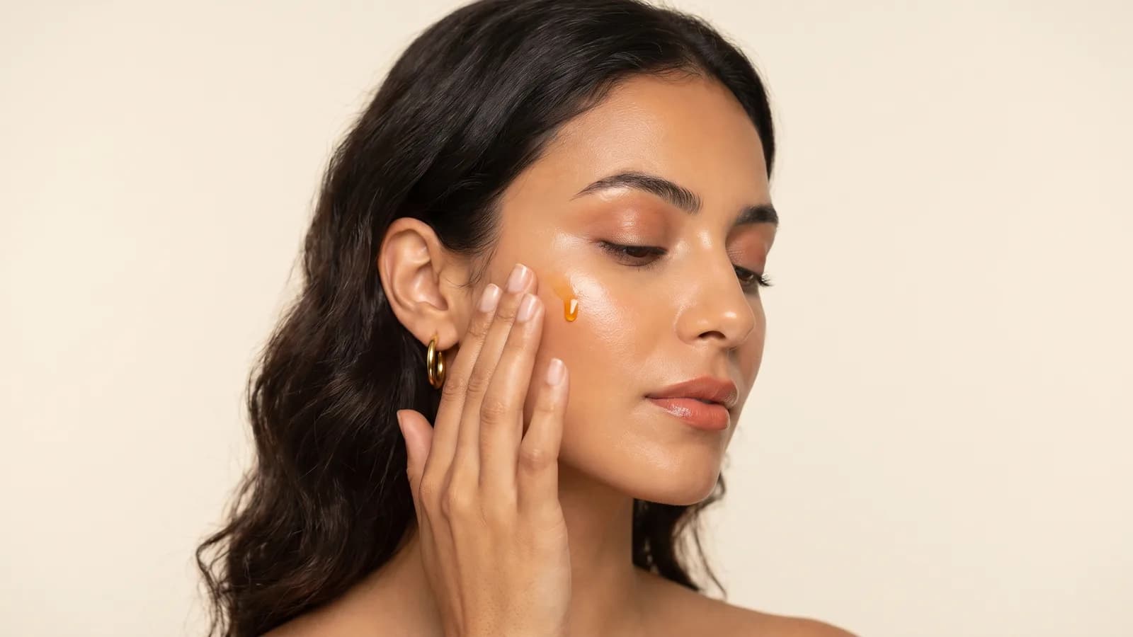 Mannequin marocaine en beauté éditoriale, teint lumineux, appliquant une goutte d’huile de soin sur la pommette