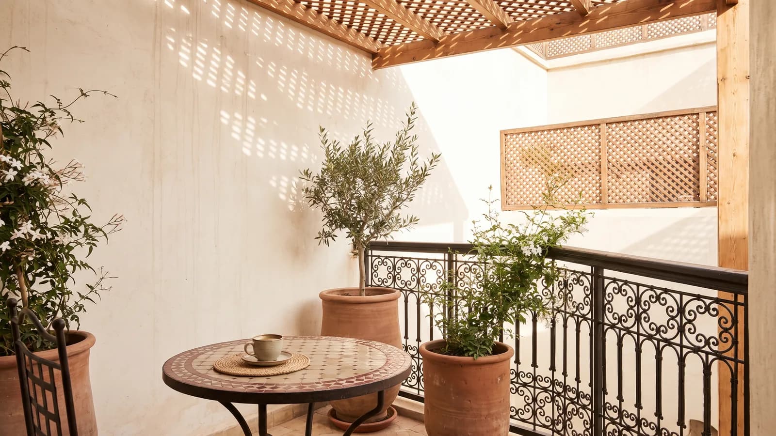 Balcon marocain au matin : table bistrot, tasse de café, jasmin et olivier en pots de terre cuite